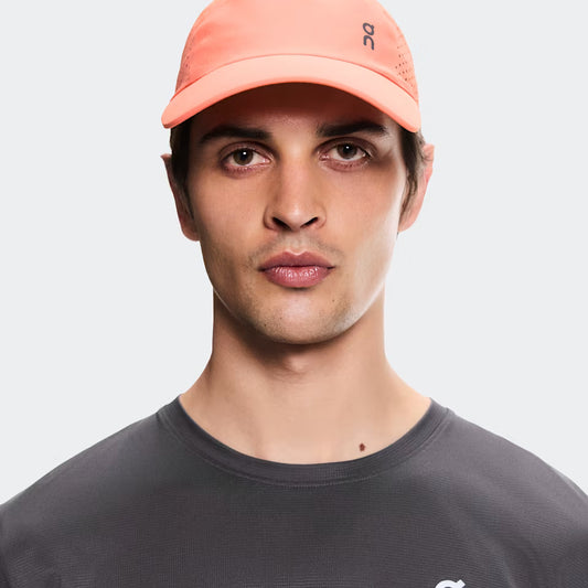 Man wearing a peach cap and gray shirt with a brand logo on a white background