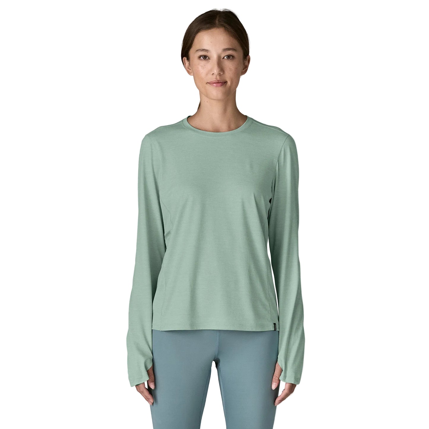 Woman wearing a light green long-sleeve shirt and gray leggings on a white background
